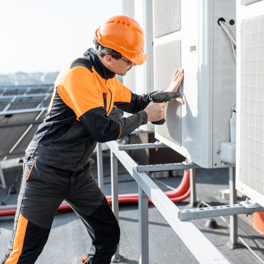 Professional workman in protective clothing installing or reparing outdoor unit of the air conditioner or heat pump on the rooftop